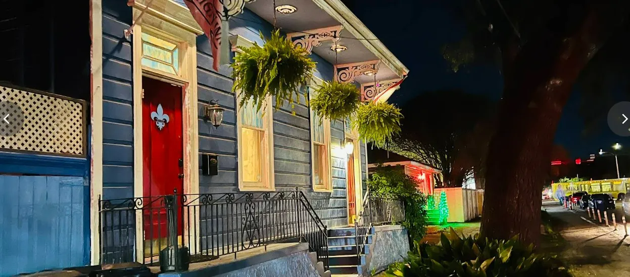Exterior of Blue60 Marigny Inn at night with blue shotgun house and red door