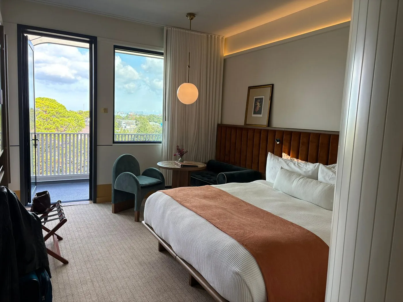 Hotel Henrietta guest room with private balcony door open to Garden District treetop views, velvet chairs, and a king bed