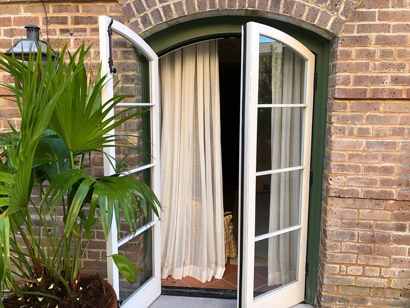 Arched French doors opening onto a balcony at Hotel Peter and Paul in the Marigny, framed by exposed brick and a tropical palm