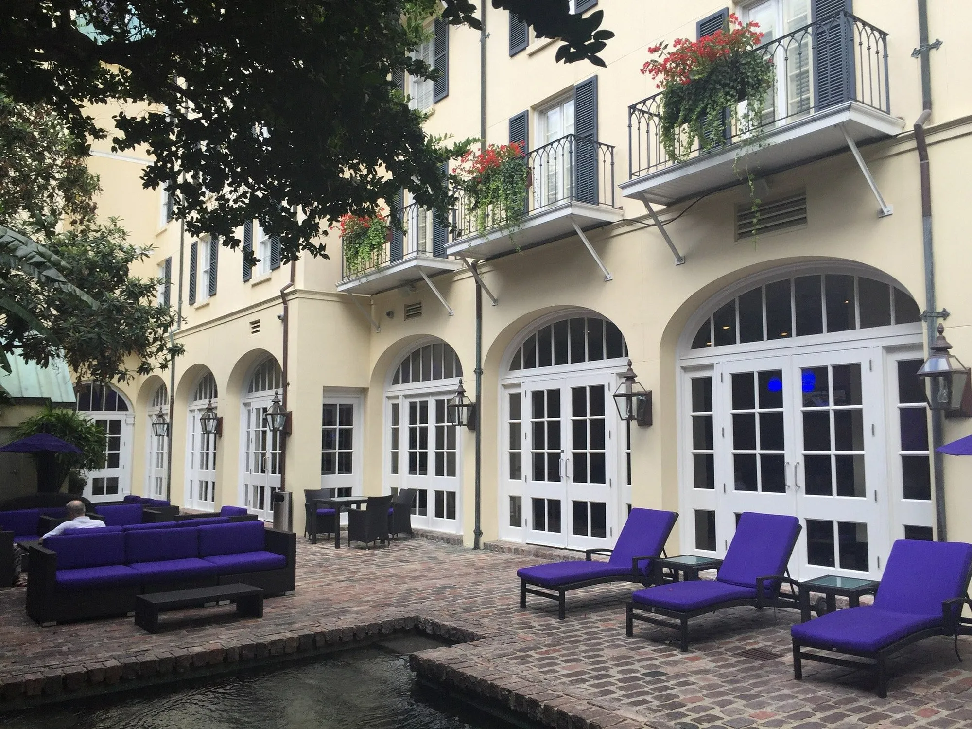 Courtyard at Hotel Le Marais with balconies draped in red flowers above cobblestone patio and blue lounge chairs